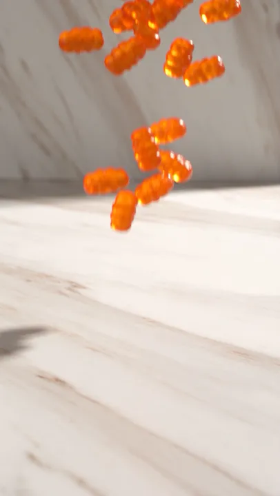 Orange gummies falling in front of white marble